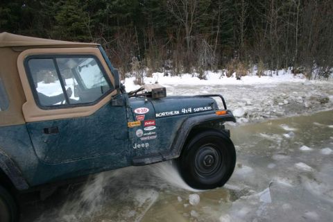 2003 Jeep TJ - A Jeep Wrangler navigates through a partially frozen body of water surrounded by trees.