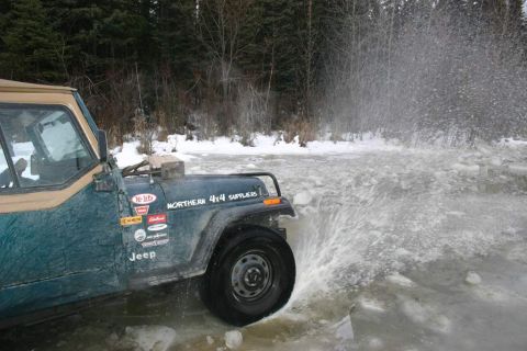 2003 Jeep TJ - A green Jeep navigates through icy water, creating a large splash. The vehicle displays several stickers, including one for Northern 4x4 Su…