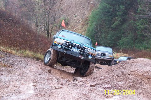 1979 Ford Bronco - Multiple off-road vehicles tackle a challenging muddy trail with steep inclines and rocky terrain.