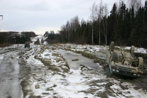 2003 Jeep TJ - A vehicle lies overturned on a muddy, icy road with another vehicle visible in the distance.