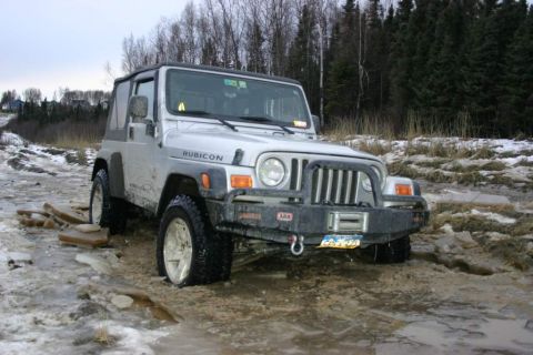2003 Jeep TJ - A silver 2003 Jeep TJ Rubicon is stuck in icy mud with trees in the background.