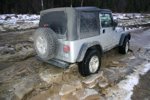 2003 Jeep TJ - Silver 2003 Jeep TJ navigates a treacherous icy and muddy road, with a spare tire mounted on the rear.