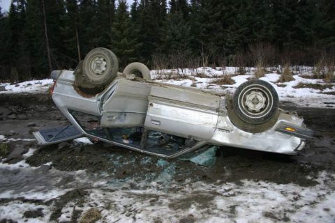 2003 Jeep TJ - Silver sedan overturned in a muddy, snowy area with trees in the background.
