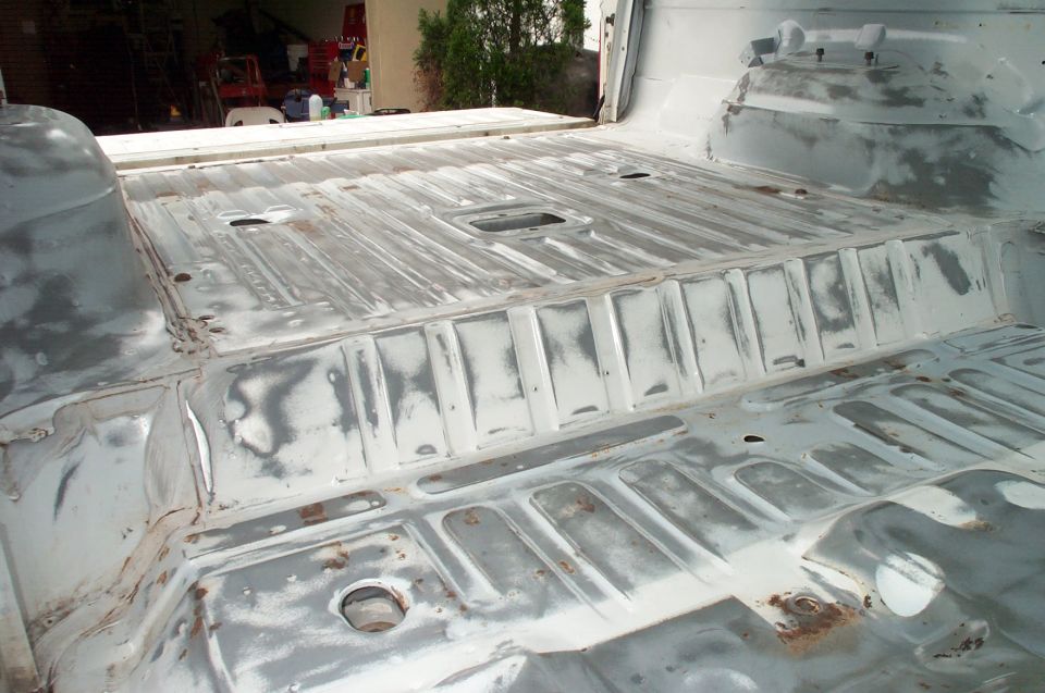 Bare and primer-coated ribbed sheet metal floor pan inside a stripped vehicle body