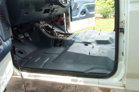 1995 Ford Bronco - Interior floor of a truck/SUV with the carpet removed and the bare floor pan coated in textured black bedliner-style spray, viewed through…
