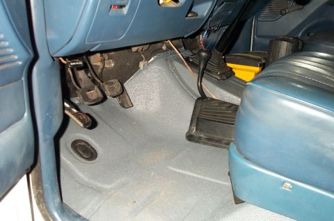 1995 Ford Bronco - Interior driver's footwell of a vehicle with blue upholstery and gray carpet, showing the brake pedal, a manual clutch pedal, and a floor-m…