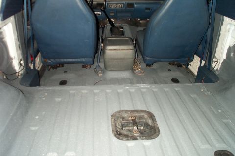 1995 Ford Bronco - Interior rear/cargo area of a Ford Bronco with the rear seats removed, showing a gray painted floor with a black access panel/cover in the…