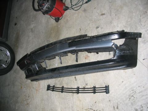 1995 Ford Taurus - A damaged car bumper and its grille are shown on a concrete surface.