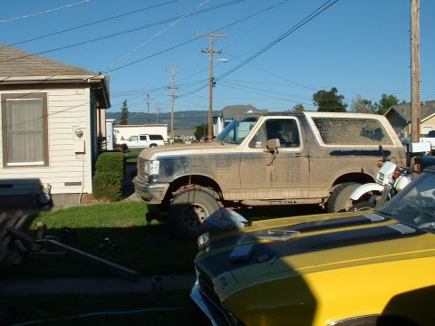 1990 Ford Bronco - A side view of a dirty 1990 Ford Bronco, parked in a residential area with other vehicles.