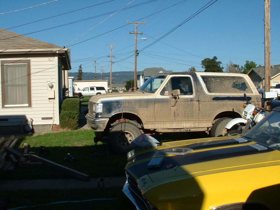 Mud-covered 1990 Ford Bronco parked next to a yellow car and a motorcycle