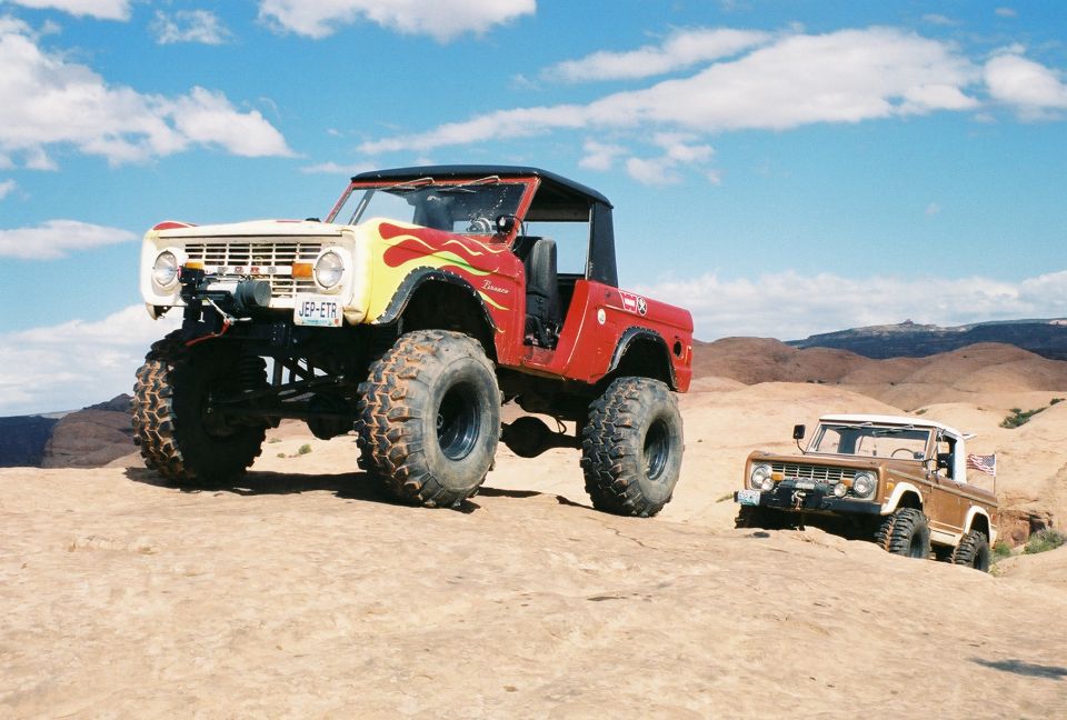 Lifted flamed Ford Bronco on big tires on slickrock, brown Bronco nearby
