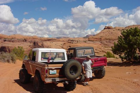 1974 Ford Bronco - Two 1974 Ford Broncos are parked in a desert landscape under a cloudy blue sky.