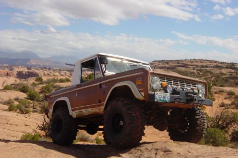 1974 Ford Bronco - A lifted 1974 Ford Bronco navigates a desert landscape under a partly cloudy sky.