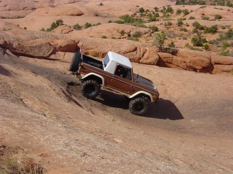 1974 Ford Bronco - A brown 1974 Ford Bronco navigates a steep, rocky terrain under a clear sky.