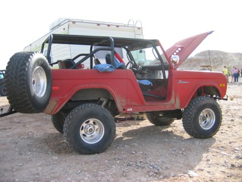 1985 Ford Bronco - This red Ford Bronco has a roll cage and the hood is open, parked outdoors.