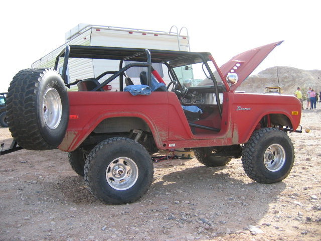 Red early Ford Bronco, side view, hood up, roll cage, lifted on mud tires
