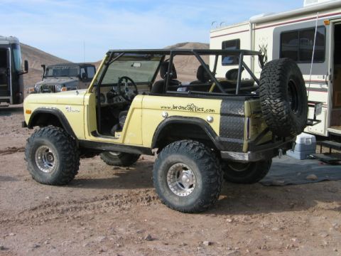 1985 Ford Bronco - Yellow 1978 Ford Bronco with roll cage and off-road tires is parked on dirt next to an RV.