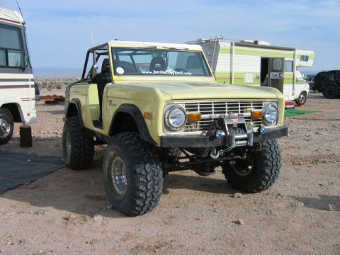 1985 Ford Bronco - This lifted Ford Bronco is parked in a desert area next to an RV and other vehicles.