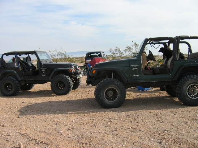 Two green lifted Jeep Wranglers parked on desert dirt with off-road tires