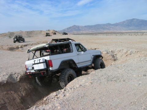 1985 Ford Bronco - Several off-road vehicles traverse a desert landscape under a clear blue sky.