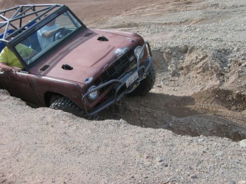 1985 Ford Bronco - This off-roading vehicle, likely a 1970s Ford Bronco, navigates a challenging dirt trench with its front tires deep in the rut.