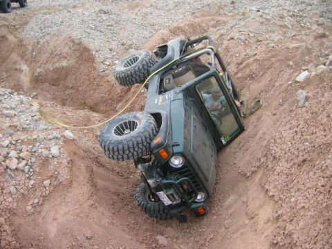 1985 Ford Bronco - A Jeep Wrangler is stuck on its side in a challenging off-road terrain, with another vehicle partially visible in the upper left corner.