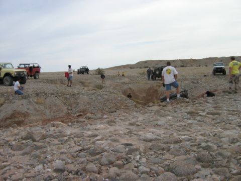 1985 Ford Bronco - Off-road vehicles gathered in a desert landscape with people observing a dug-out area.