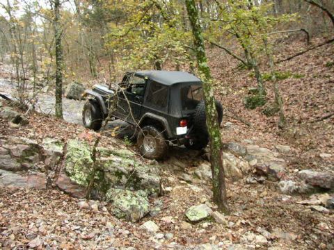 1995 Ford Bronco - A black Jeep Wrangler TJ tackles a challenging off-road trail with large rocks and fallen leaves.