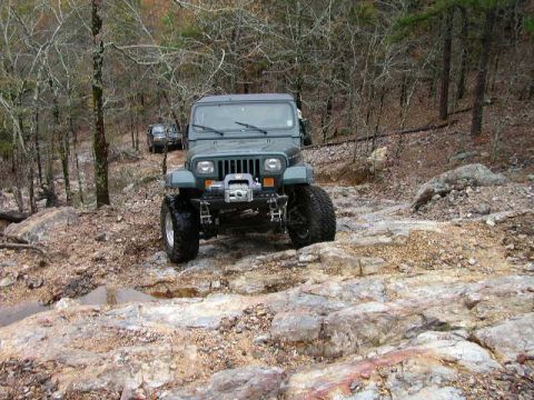 1995 Ford Bronco - Two Jeep Wranglers tackle a challenging off-road course in a wooded area.
