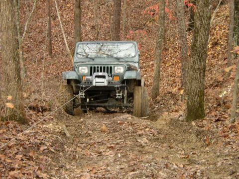 1995 Ford Bronco - A Jeep Wrangler navigates a challenging off-road trail through a wooded area during autumn.