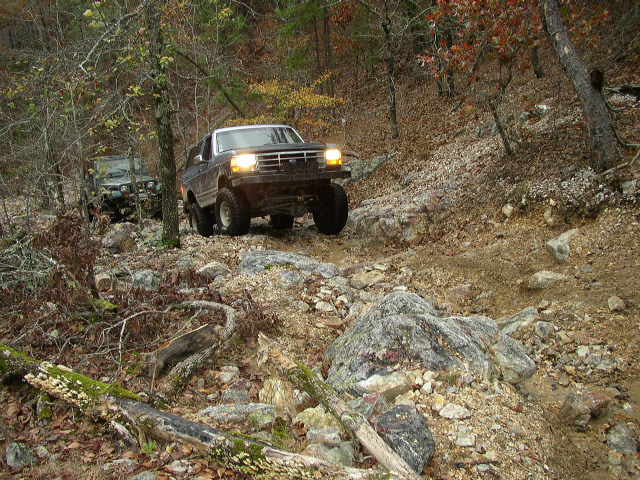 Ford Bronco and another SUV driving on a rocky, wooded trail