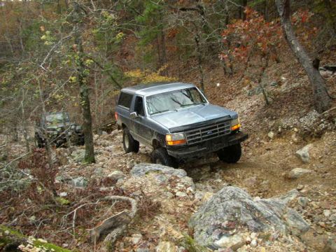 1995 Ford Bronco - 1995 Ford Bronco navigates a challenging rocky path in a wooded area.