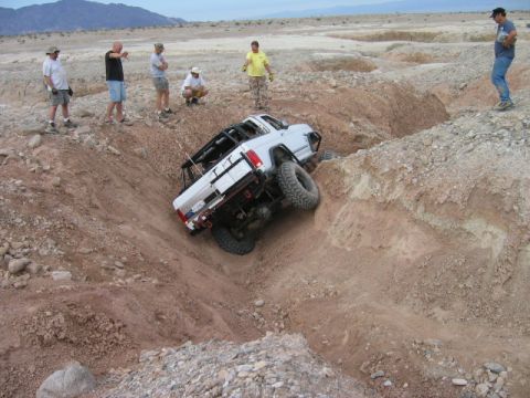 1985 Ford Bronco - White off-road truck with roll cage is stuck in a steep dirt ravine.