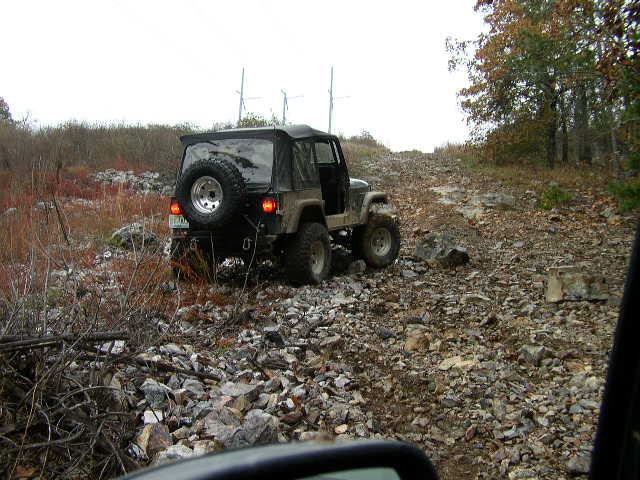 Jeep Wrangler driving up a rocky hill, spare tire mounted on the back