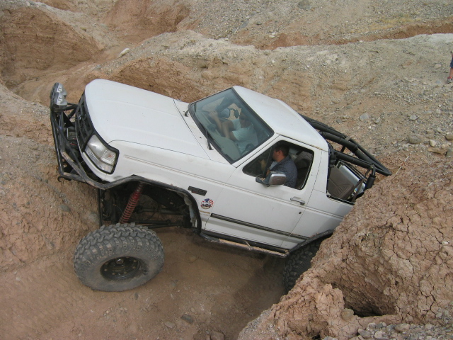 White lifted Ford Bronco on oversized tires climbing rocks off-road