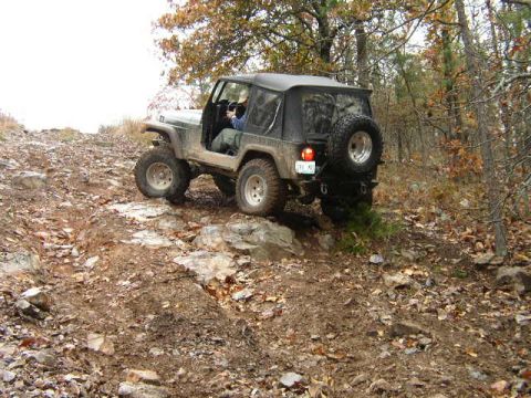 1995 Ford Bronco - A black Jeep Wrangler TJ navigates a challenging rocky terrain in a wooded area.
