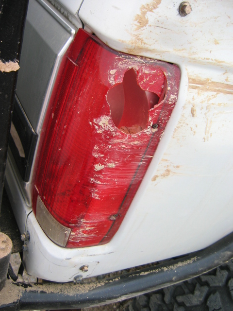 1985 Ford Bronco - Close-up of a damaged rear taillight on a white SUV, showing significant wear and tear.
