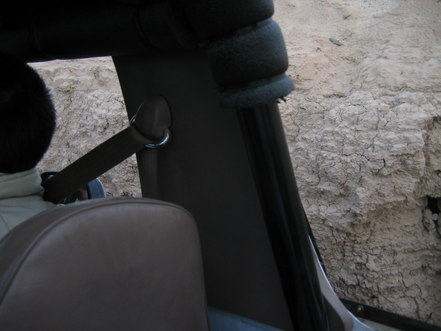 Vehicle interior with brown seat and seatbelt, dirt wall visible outside window