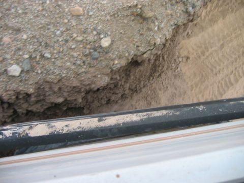 1985 Ford Bronco - A view from inside a vehicle shows a black roof rack coated in dirt and sand, overlooking a sandy embankment.