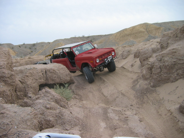 Red doorless Ford Bronco descending a steep sandy desert trail