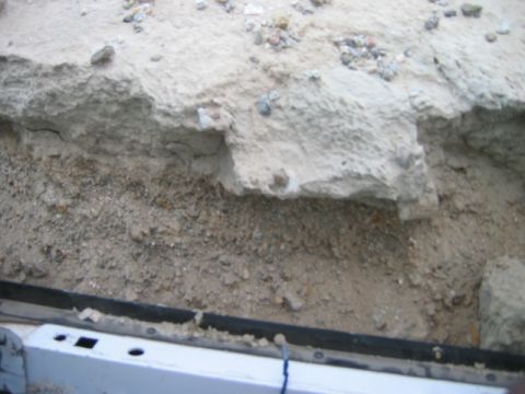 1985 Ford Bronco - Dirt embankment with rocks and soil, viewed from above a white vehicle part. Supermotors.net logo visible.