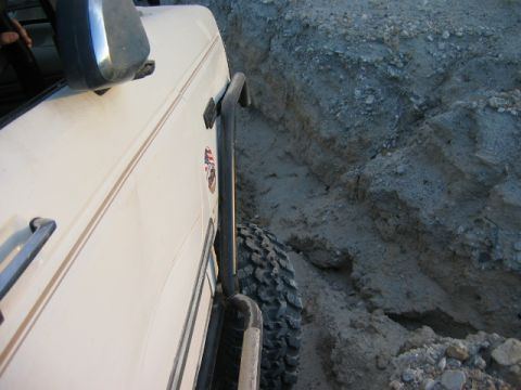 1985 Ford Bronco - White SUV navigates a rocky, off-road terrain from a side perspective.
