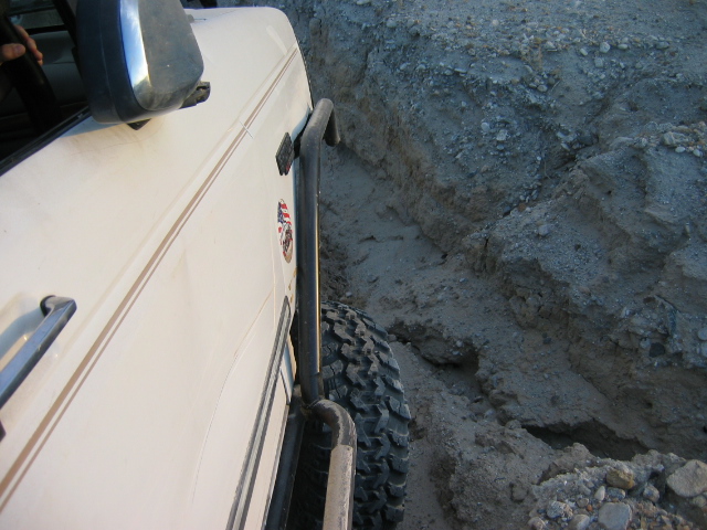 White SUV with tube rock sliders and mud tire in a deep dirt rut off-road