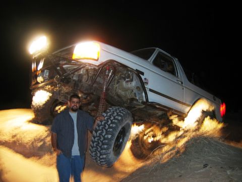 1985 Ford Bronco - A man poses with his heavily modified SUV as it kicks up dirt and sparks during an off-road excursion at night.