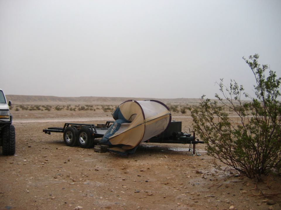 Tandem-axle utility trailer with collapsed tent in a hazy desert setting