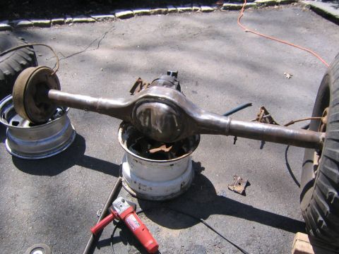 1978 Ford Bronco - A rear axle assembly is shown resting on rims, with a grinder and other parts scattered around.