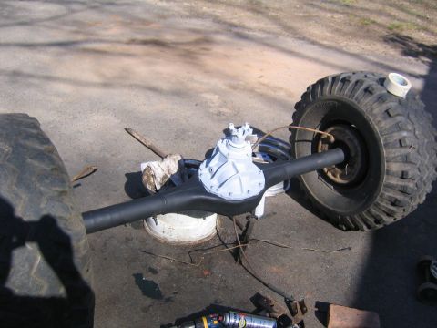 1978 Ford Bronco - A rear axle housing painted flat black with a freshly painted white/silver third-member differential carrier, resting on a white wheel used…