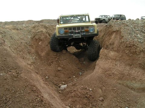 1985 Ford Bronco - Modified Ford Bronco tackling rough terrain off-road. Multiple vehicles are present in the background.