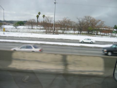 1985 Ford Bronco - Cars drive on a highway with snow covering the landscape under a cloudy sky.