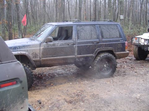 1993 Ford Bronco - Two off-road vehicles navigate a muddy trail in a wooded area.